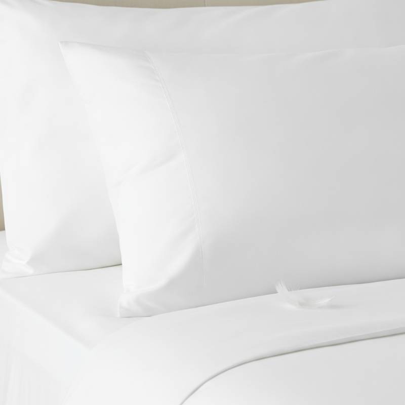 A close-up photo of a fluffy duck feather pillow on a white bed sheet showing its soft texture