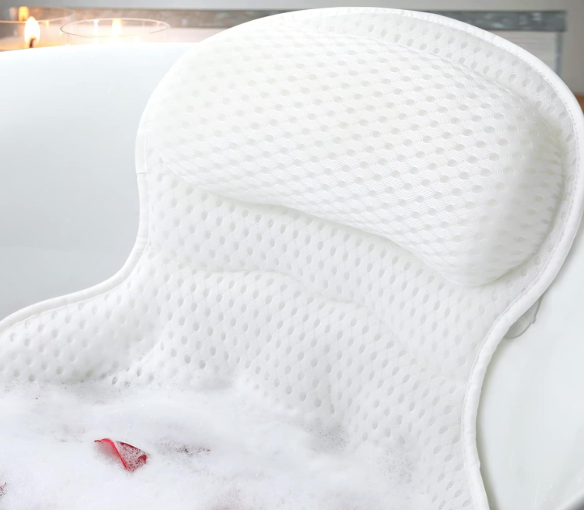 A person relaxing in a white bathtub with a soft white bath pillow supporting their neck